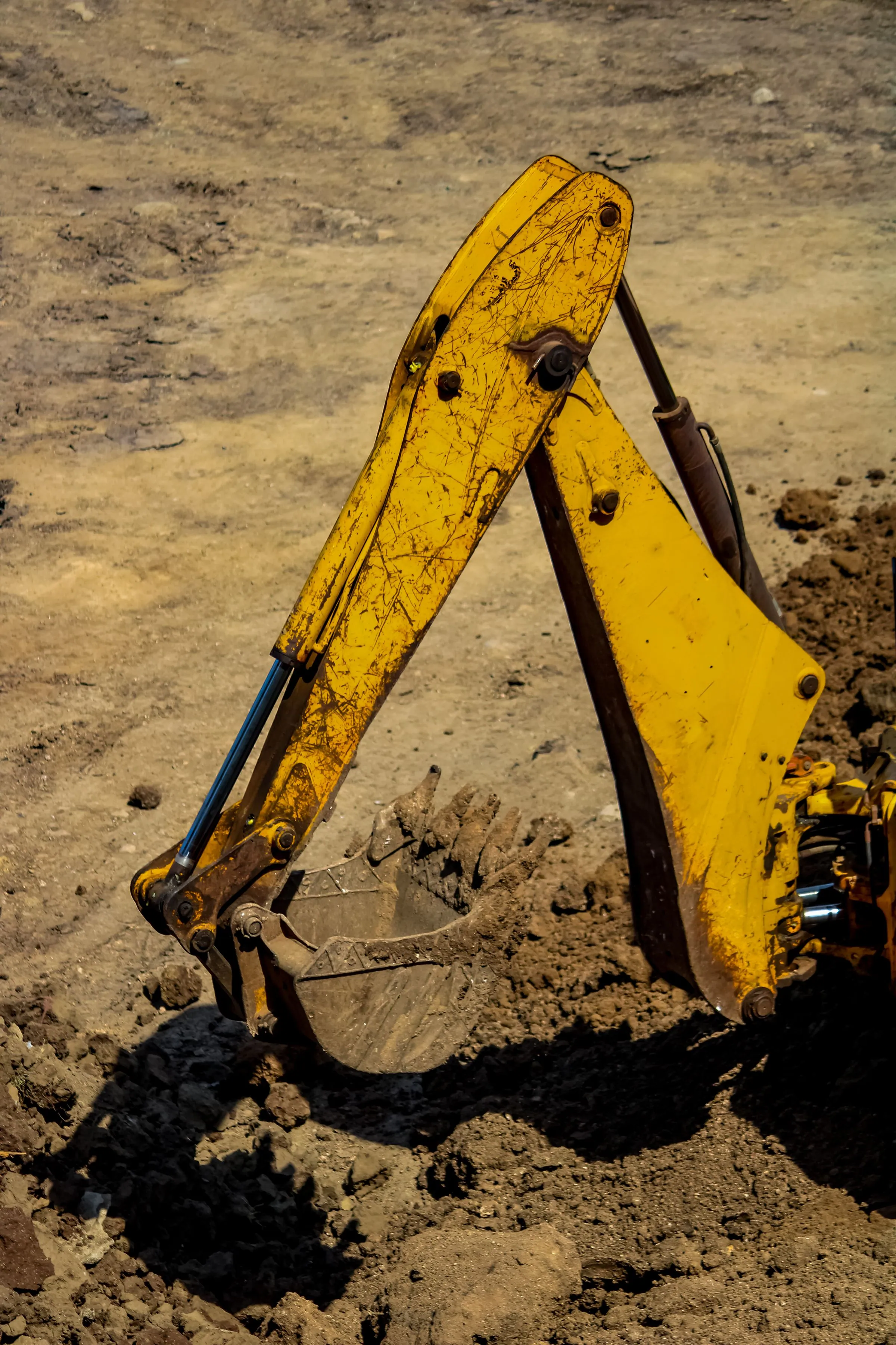 Yellow excavator arm and toothed bucket digging into loose brown earth on a bare site