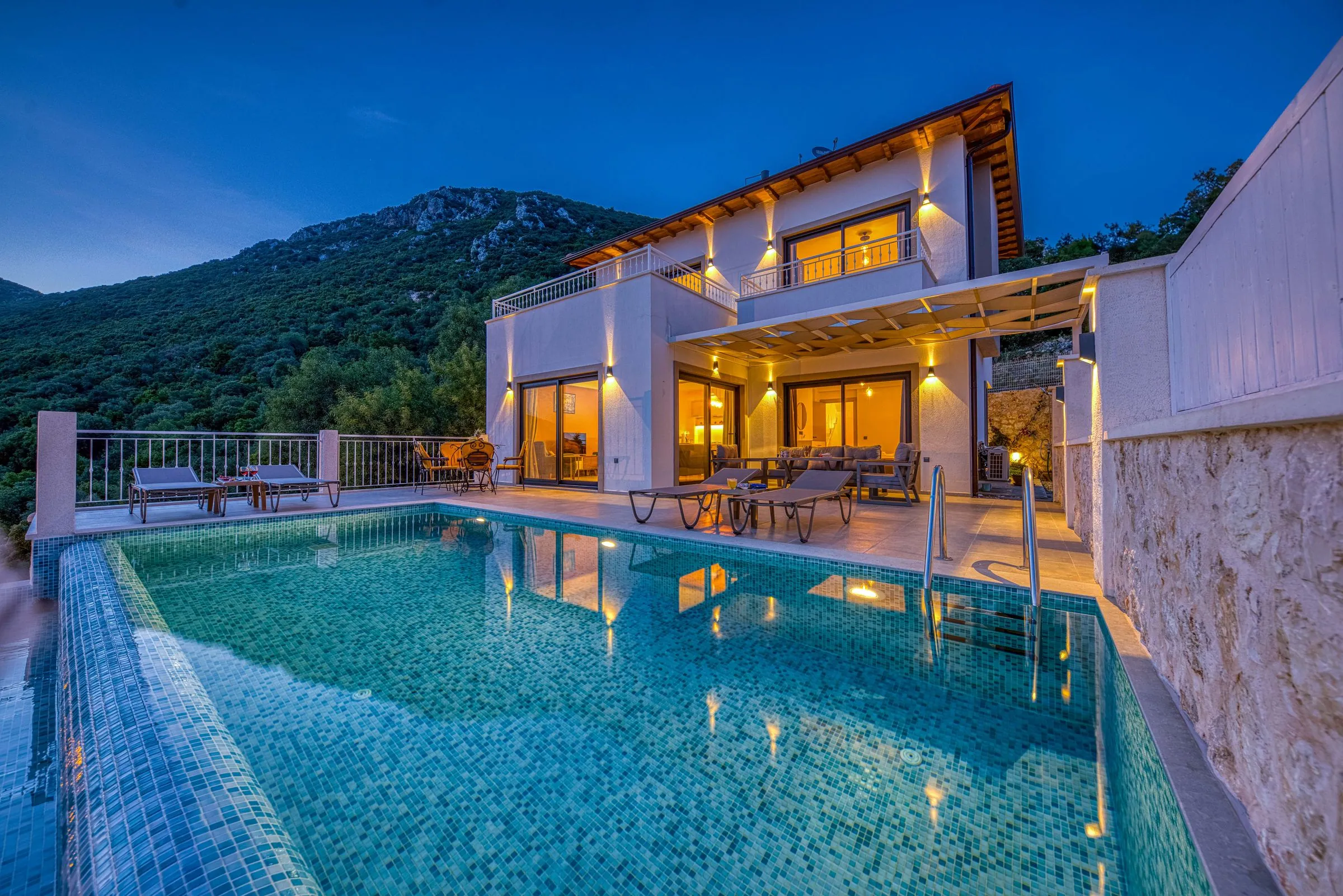 The same pool and villa after dark, underwater lights on and the interior glowing warm through the glass doors