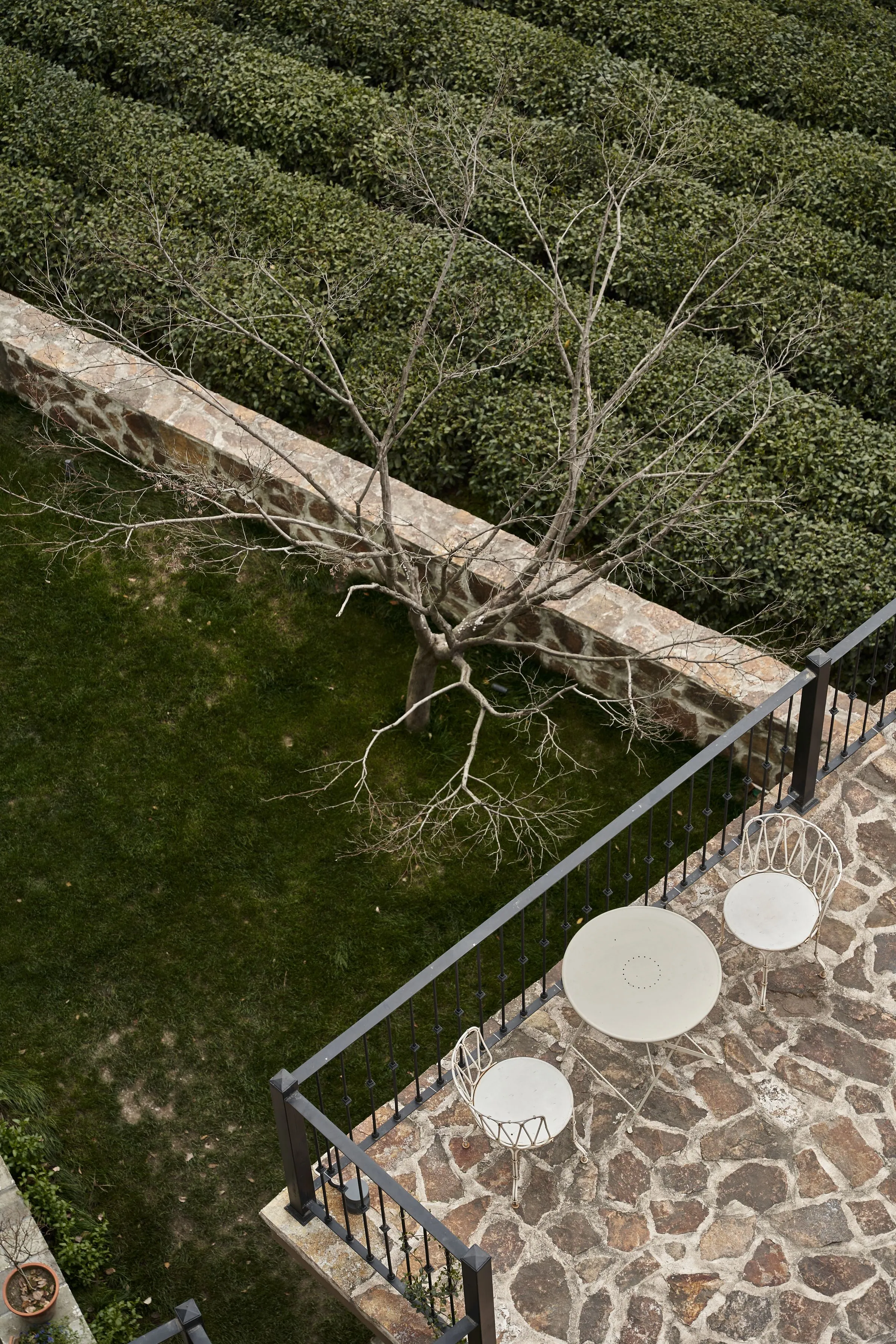 Paved stone terrace running alongside a planted garden bed with shrubs and greenery