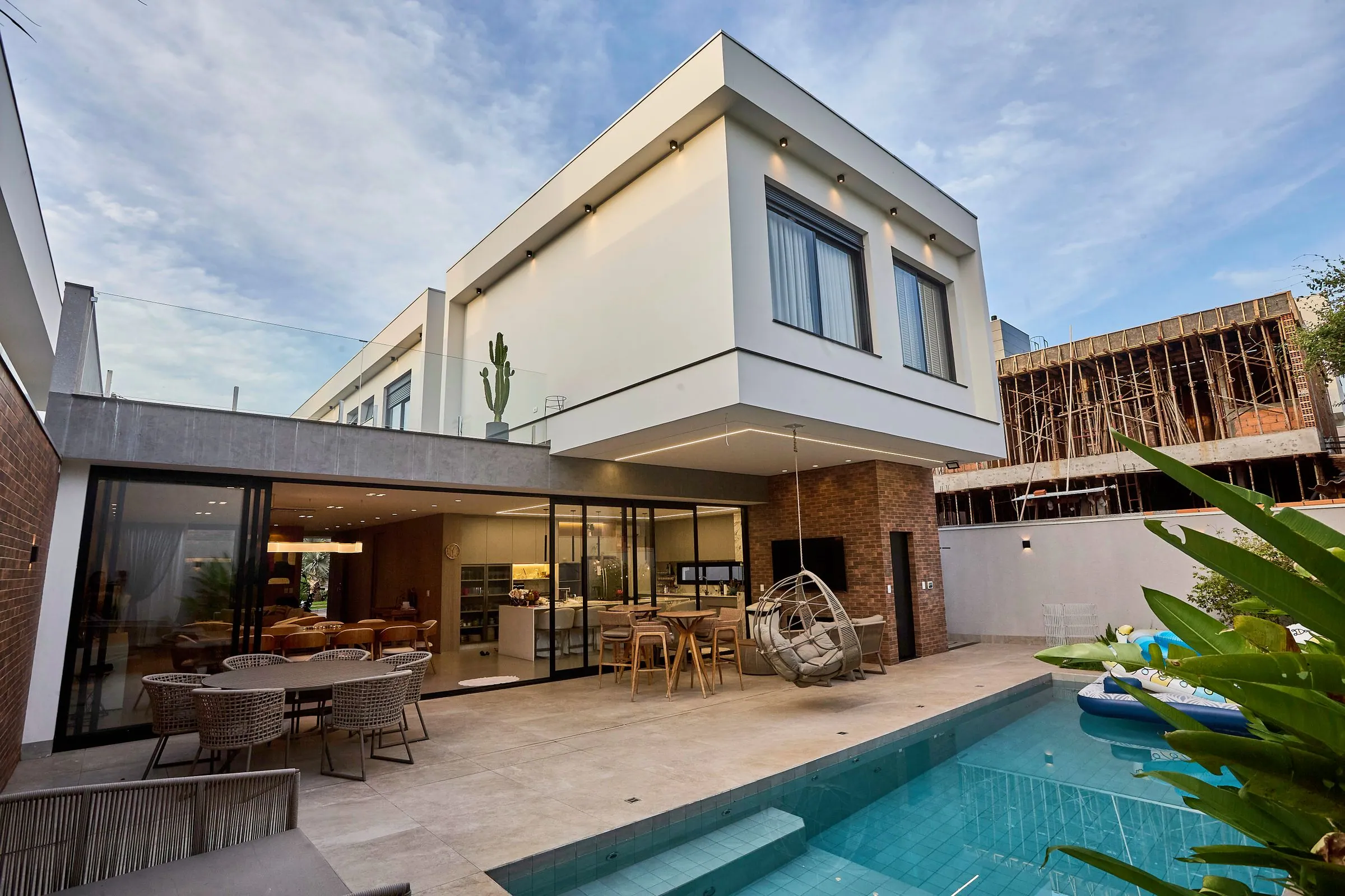 Flat-roofed two-storey house with a cantilevered upper floor, a covered dining area behind glass sliding doors, and a pool along the right side