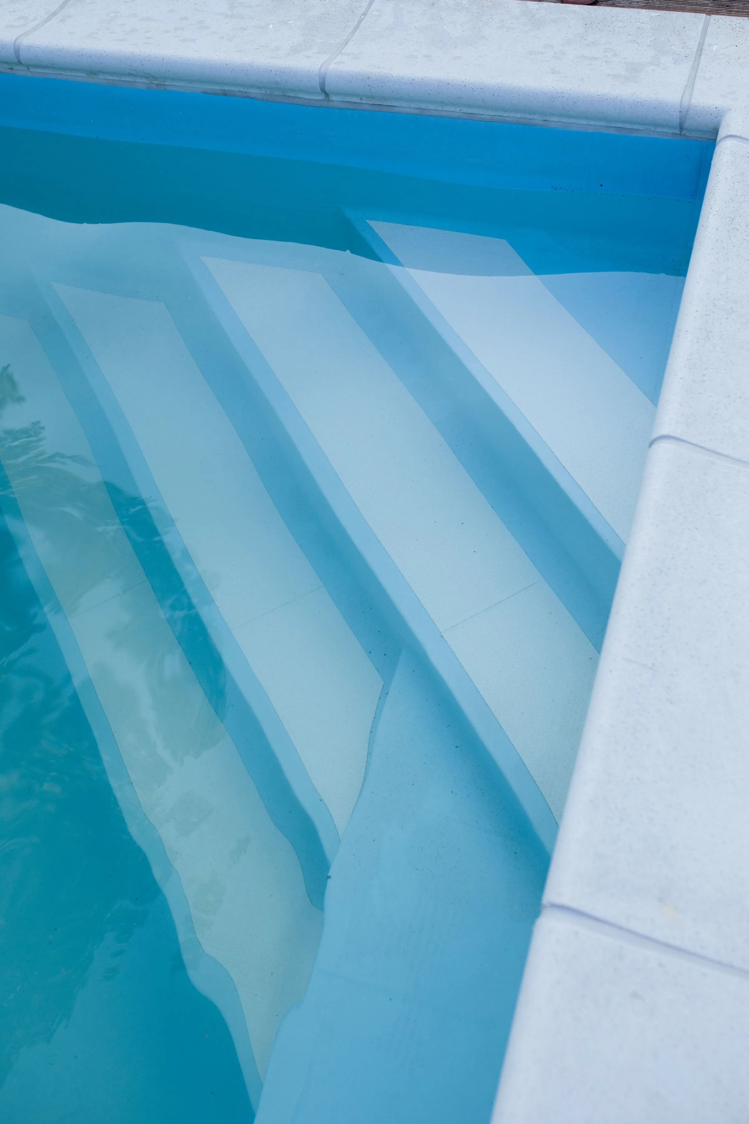 Close view of wide shallow entry steps under clear blue pool water, with pale stone coping along the edge