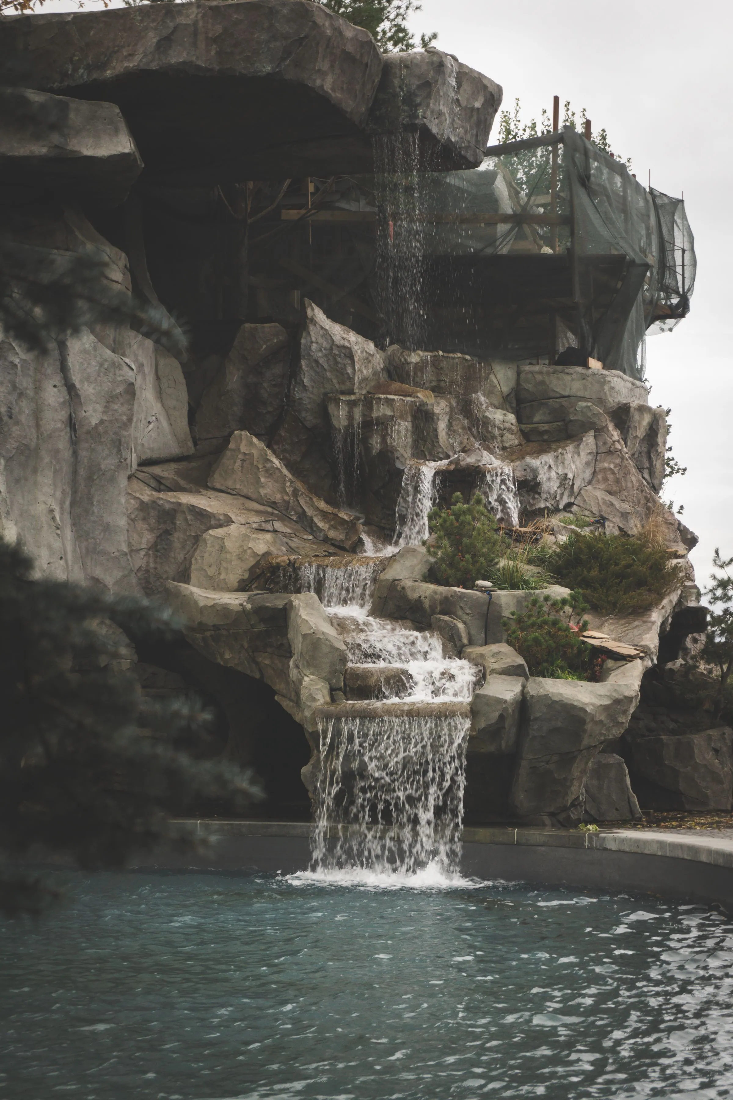 Constructed rock waterfall with several stepped cascades falling into a pool with visible coping at the base