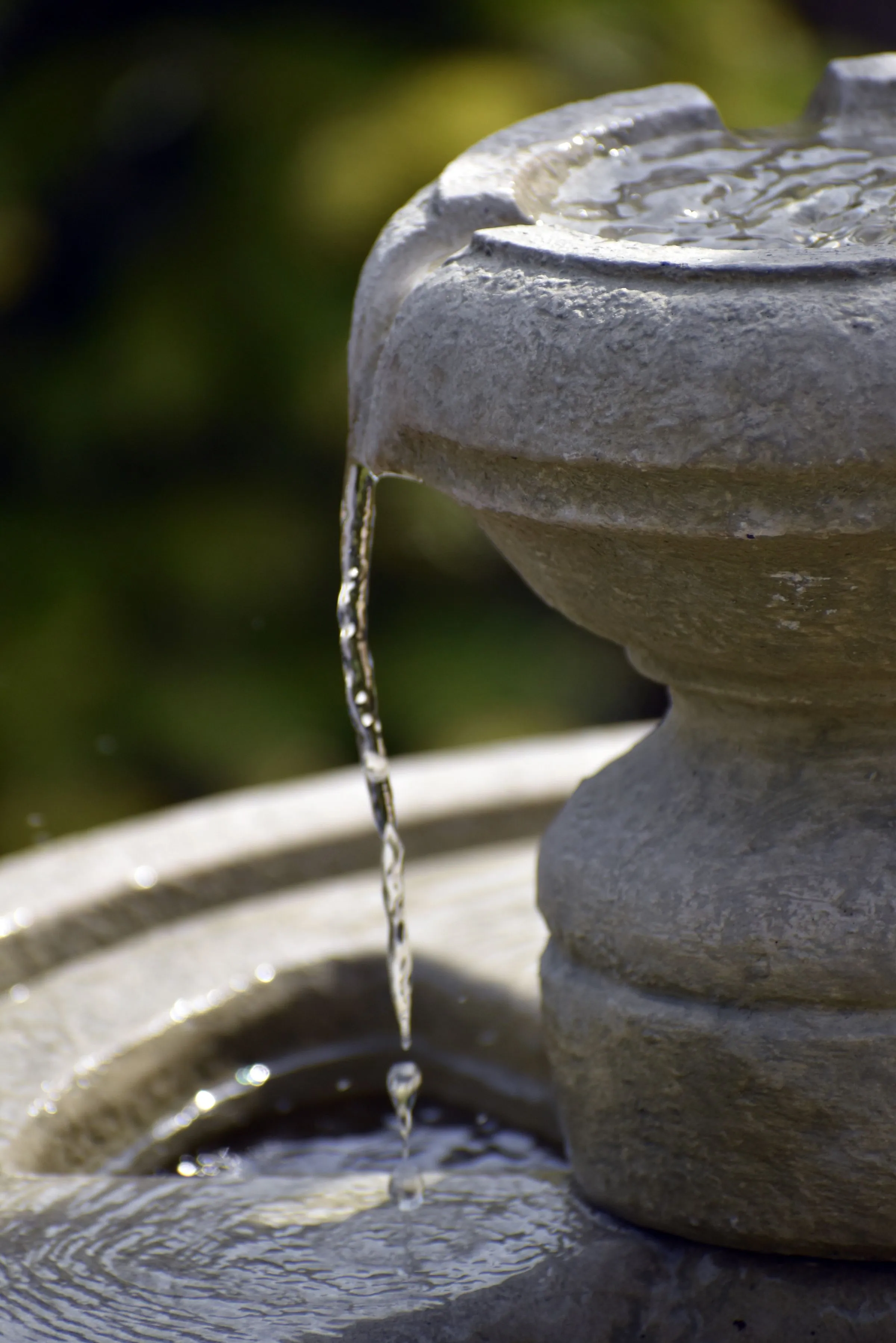 Close-up of water spilling in a thin stream from the upper tier of a grey stone fountain into the basin below